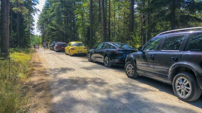 Bilar parkerade längs sandväg.
