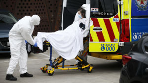 Rekordmånga har dött i delstaten under det senaste dygnet. Ambulanspersonal i skyddsutrustning lyfter in en kvinna på bår i ambulans i Victoria, Australien.