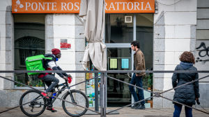 Ett cykelbud väntar på ett uppdrag utanför en restaurang i det coronadrabbade Milano. Ett cykelbud väntar på att leverera mat i Milano mitt under coornaepidemin.
