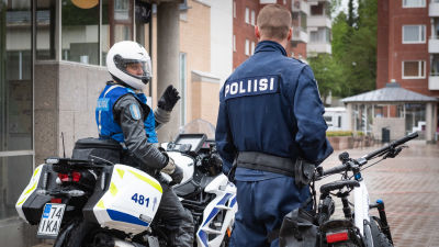 En polis sitter på en motorcykel, medan en annan polis står vid en cykel.