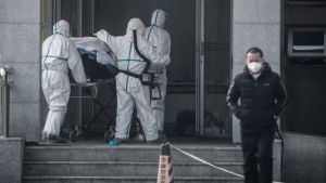 En patient som misstänks ha drabbats av virusrelaterad lunginflammation bars in på Jinyintan-sjukhuset i Wuhan på lördagen den 18.1. Tre personer i vita dräkter rullar in en patient på en bår i en byggnad.