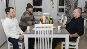 Stödgrupp för pappor vid kaffebordet. Mikko Karhukorpi har ett barn, tvåbarnspappan och ledaren Pekka Pudas och fyrabarnspappan, journalisten Kaje Komulainen. Tre män sitter vid ett matbord.