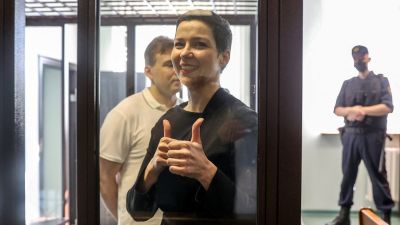 Miaria Kolesnikova visar tummen upp-tecken under rättegången mot henne. I bakgrunden står hennes medåtalade Maxim Znak.