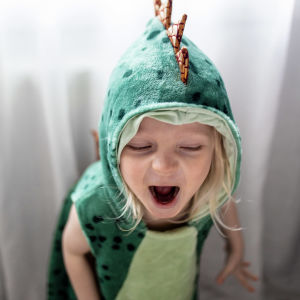 Leikki-ikäinen lapsi karjuu dinosaurusasu päällään.