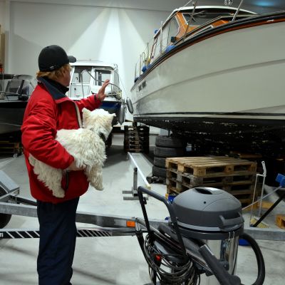 hamnkapten Göran Berghem med hunden Nappi i famnen betraktar en av båtarna i båtförvaringshallen vid Baggö Marina.