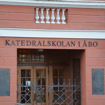 Ingången till Katedralskolan i Åbo. Byggnaden är röd med trädörrar och en järngrind.