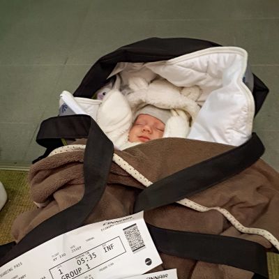 En baby i sin vagn. Ovanpå vagnen ligger två flygbiljetter.