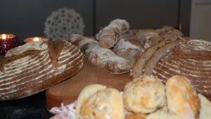 Det här surdegsbrödet är enkelt för nybörjare. Ett skärbräde med hembakt bröd i olika utformning, några ljusa semlor med frön på, några grovt tvinnade baguetter och limpor som snittats för vackra mönster.