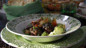 En portion lammgryta med mos och romanesco garnerad med finklippt persilja. Portionen är serverad i en djup tallrik som är vit med en grön bård.