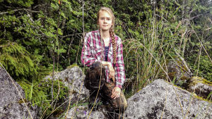 Anni Selenius är praktikant på Österbottens Fiskarförbund. Kvinna i vildmarkskläder sitter på mossbeklädda stenar i skog.
