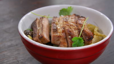 En röd skål med en portion nudelsallad. Högst upp på portionen ligger en bit uppskuret kött toppad med gröna örter.