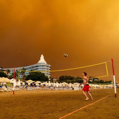 Någon spelar volleyboll på en strand i Turkiet. Himlen är orange och full av rök.