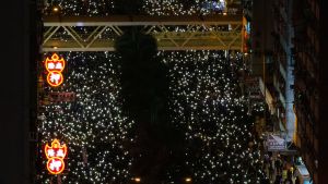 Då mörkret föll tände deltagarna ljuset på sina telefoner för att visa hur många de var. Människor håller uppe sina telefoner som ljus i en demonstration i Wan Chai i Hongkong söndagen den 8 december.
