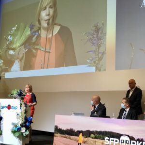 SFP-ordförandeAnna-Maja Henriksson tacka för återvalet. Dessutom valdes 3 viceordförande och 23 medlemmar i partifullmäktige. Anna-Maja Herniksson i talarstol och på storskärm med blombukett vid partidagen.