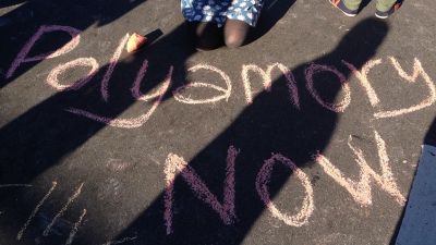 Texten Polyamory now står skrivet med krita på asfalt.