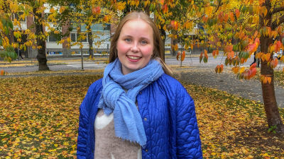 Porträtt på Veronica Helanen utomhus med färggranna höstlöv i bakgrunden.