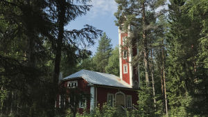 Puiden latvojen läpi piirtyy esiin torni. Varjakansaaren vanhan sahakylän paloasema, punavalkoinen rakennus jossa torni, metsän keskellä.