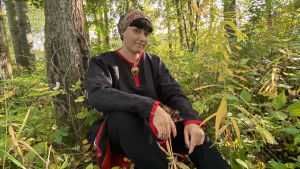 Maura Häkki. På bilden syns Maura Häkki som sitter och poserar i ett skogslandskap.