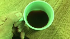 Kaffet ändrar färg i det gröna ljuset. En kaffekopp i en grönfärgad omgivning.