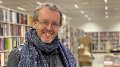 En leende man med glasögon framför rader av bokhyllor.