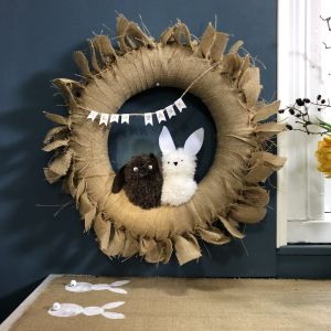 Kransen kan givetvis göras i andra färger och med annat tyg om du så tycker. Krans med kaniner av garnbollar och en duk med kanintryck på.