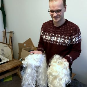 Det är svårt att hitta bra tomteskägg nu för tiden, berättar Filip Nyman. Det företag de tidigare beställde av gick i konkurs. Här är det vänstra skägget gjort av plastfiber och det högra av naturfiber, vilket gör att det högra ser mer verklighetstroget ut. en kille håller i två vita krulliga tomteskägg