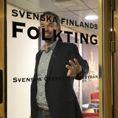 Markus Österlund öppnar glasdörr med texten Svenska Finlands Folkting.