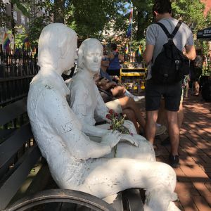 Statyer och parkbänkar för dem som vill minnas Stonewallupproret Två vita, sittande statyer i Christopher Park, med blommor i famn, personer som ledde Stonewallupproret
