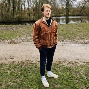 Ollie Charlton hoppas kunna stanna i Nederländerna. 23-åriga studeranden Ollie Charlton i fotograferad i en park i Amsterdam. Han är ledigt klädd. Det är fortfarande tidig vår och inga löv i träden.