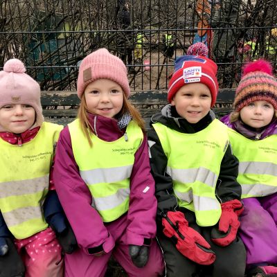Fyra dagisbarn med gula reflexvästar på ute på parkbänk.