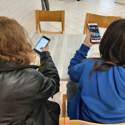 Två flickor sitter vid lunch med sina mobiltelefoner.