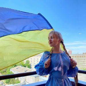 Ung blond kvinna med flätor med Ukrainas flagga bakom sig