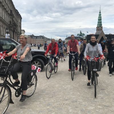 Mette Frederiksen cyklar med röda små flaggor fästa på cykelkorgen.