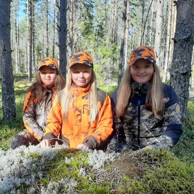 Tre flickor i jaktkläder i skogen.