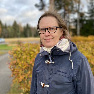 Kyläasiamies Elina Leppänen katsoo hymyillen kameraan sininen takki yllään. Taustalla ruskan värjäämiä pensaita.Tuuloksessa 4.10.2021.