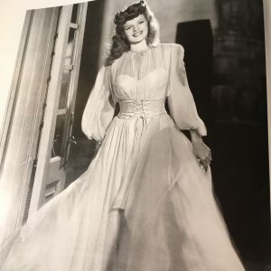 Rita Hayworth på 1940-talet, i valkfrisyr och vit chiffongklänning. Rita Hayworth i klädd en vit chiffongklänning.