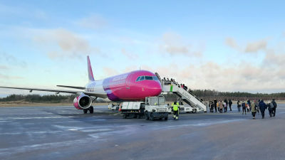 Passagerare går på ett flygfält fram till ett rosa-lilafärgat flygplan.