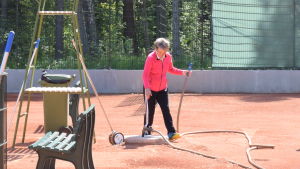 Barbro Wikberg har många järn i elden. Här vattnar hon en av tennisbanorna i Hangö. En kvinna på tennisplan. Hon spelar inte utan har just vattnat planen. Vattenslangen ligger på marken.