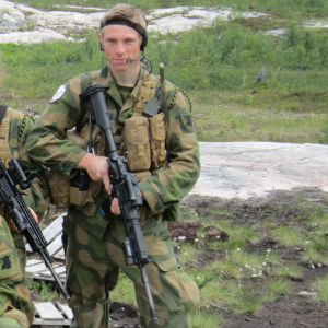 Erling Søyland tjänstgjorde i Norges militär 2010-2011. En man i militäruniform står på ett gräsbelagt fält. Han ser bestämt in i kameran. Han håller i ett stormgevär.