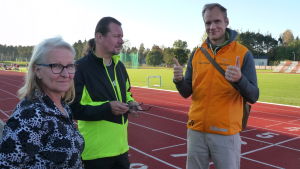 Mirja och Arto i startgroparna, Heikki tipsar och hejar. Mirja Koponen och hennes man Arto samt idrottsinstruktör Heikki Kiili på Karis idrottsplan en solig kseptemberkväll. Heikki visar tummen upp.