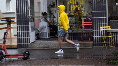 En man i gul regnrock promenerar i regn i Berghäll i Helsingfors.