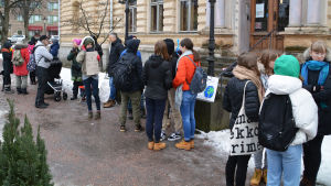 På fredagens klimatdemonstration utanför stadshuset i Borgå hade relativt många slutit upp trots allt. På plats fanns barn, unga och vuxna i olika åldrar, bland annat flera studerande från Linnanjoen lukio. Ett tjugotal unga människor står utanför stadshuset i Borgå, ett gult stenhus.