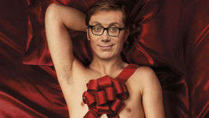 Hello Ladies - The Movie. Mies makaa punaisella silkkilakanalla juhlakoriste päällään.