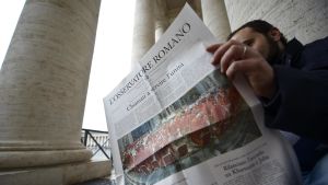 En man sitter och läser tidningen L'Osservatore Romano. Bilden är tagen år 2013. En man läser en upplaga av tidningen L'Osservatore Romano. Bilden är tagen 2013.