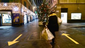 Julshopping i Genua. Kvinna med shoppingkassar går på mörk gata i Italien. Mitt på gatan står en julgran.