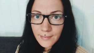 Lena Enlund har sett flera närvårdare byta bransch på grund av lönen. Kvinna med mörkt hår och glasögon sitter lutad mot en vägg.