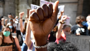 De antirasistiska demonstrationerna som ordnats den senaste tiden är de största i modern historia, skriver Minna Salami. På bilden syns en knuten hand i förgrunden, i bakgrunden syns flera människor som håller upp en knuten näve och håller i plakat. Många är iklädda ansiktsskydd.