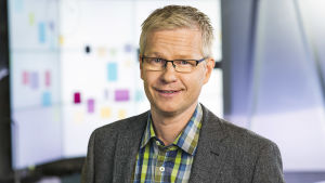 hymyilevä silmälasipäinen mies katsoo kohti