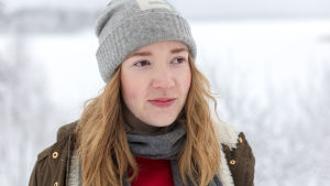 Nuori nainen seisoo lumisessa talvimaisemassa pipo päässä.