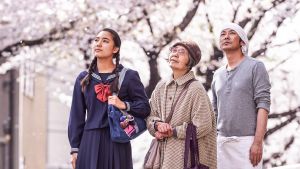 Kirsikkapuiden alla on japanilainen elokuva katukeittiön pitäjästä ja vanhasta rouvasta. Kaksi naista ja mies seisovat kirsikkapuiden alla.